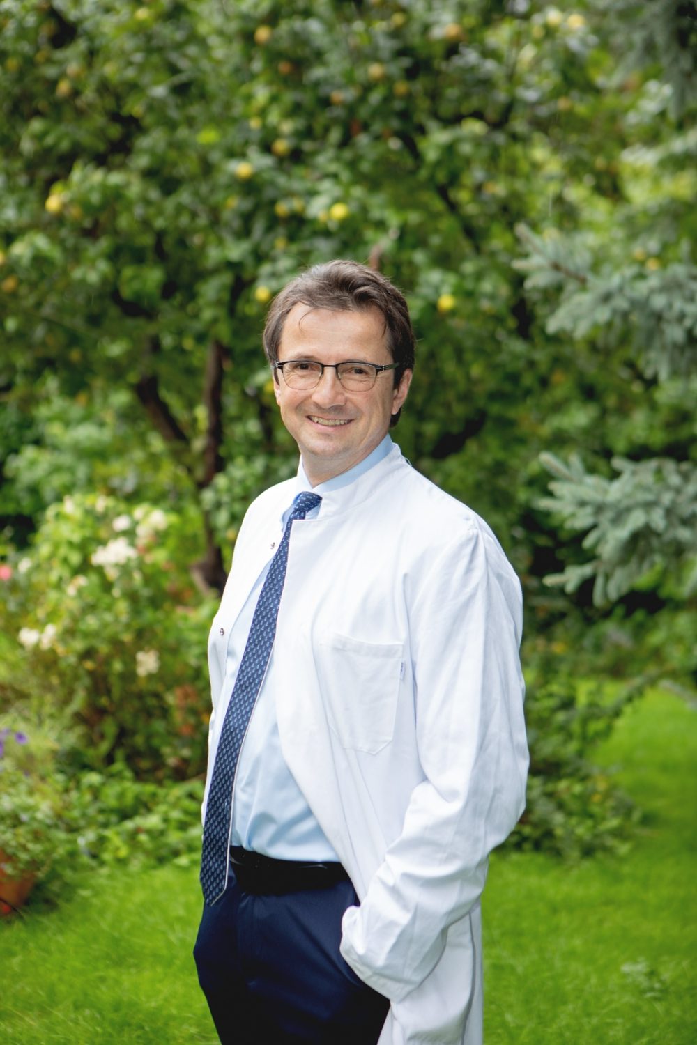 Prof. Dr. med. Peter E. H. Schwarz im weißen Arztkittel, im Freien vor Bäumen und Wiese.