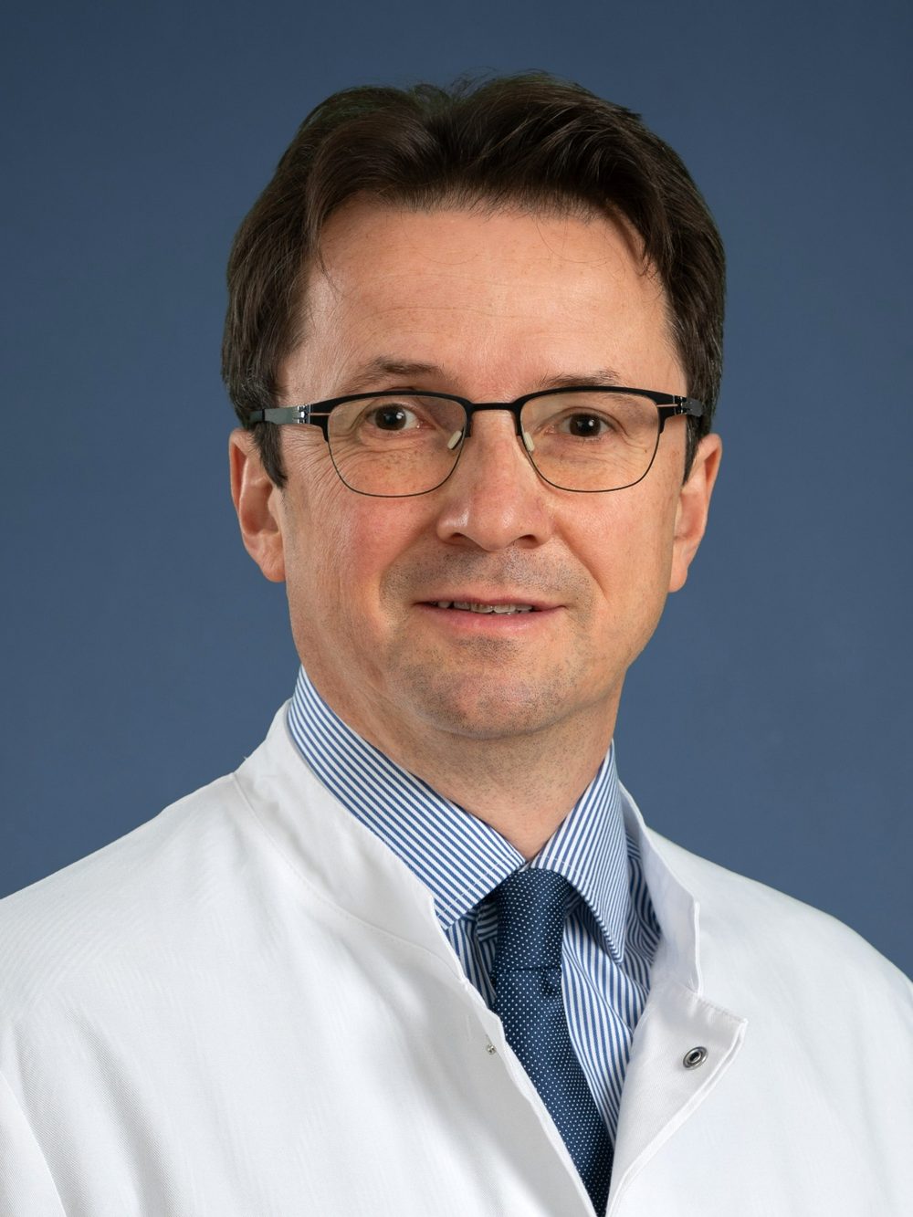 Porträt von Prof. Dr. med. Peter E. H. Schwarz im weißen Arztkittel vor blauem Hintergrund.