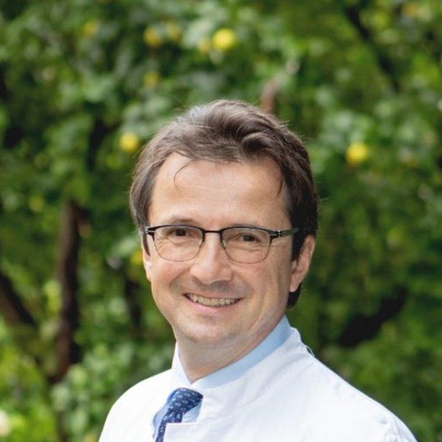 Prof. Dr. med. Peter E. H. Schwarz im weißen Arztkittel im Garten, blickt in die Kamera.